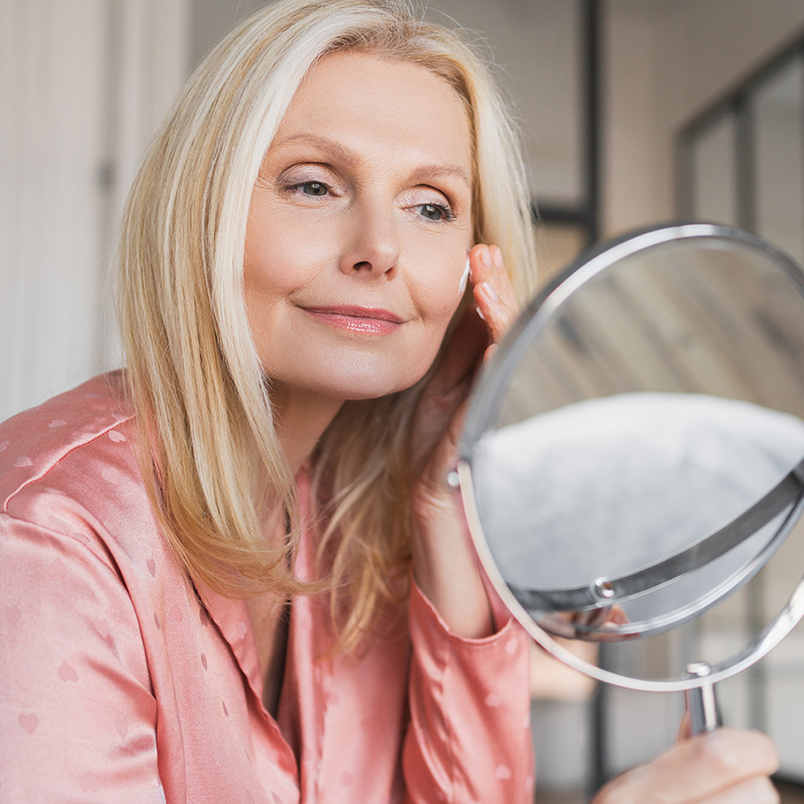 Mature woman in pink looking at herself in the mirror