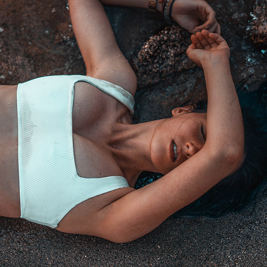 a woman in a white swim suit laying in the sand
